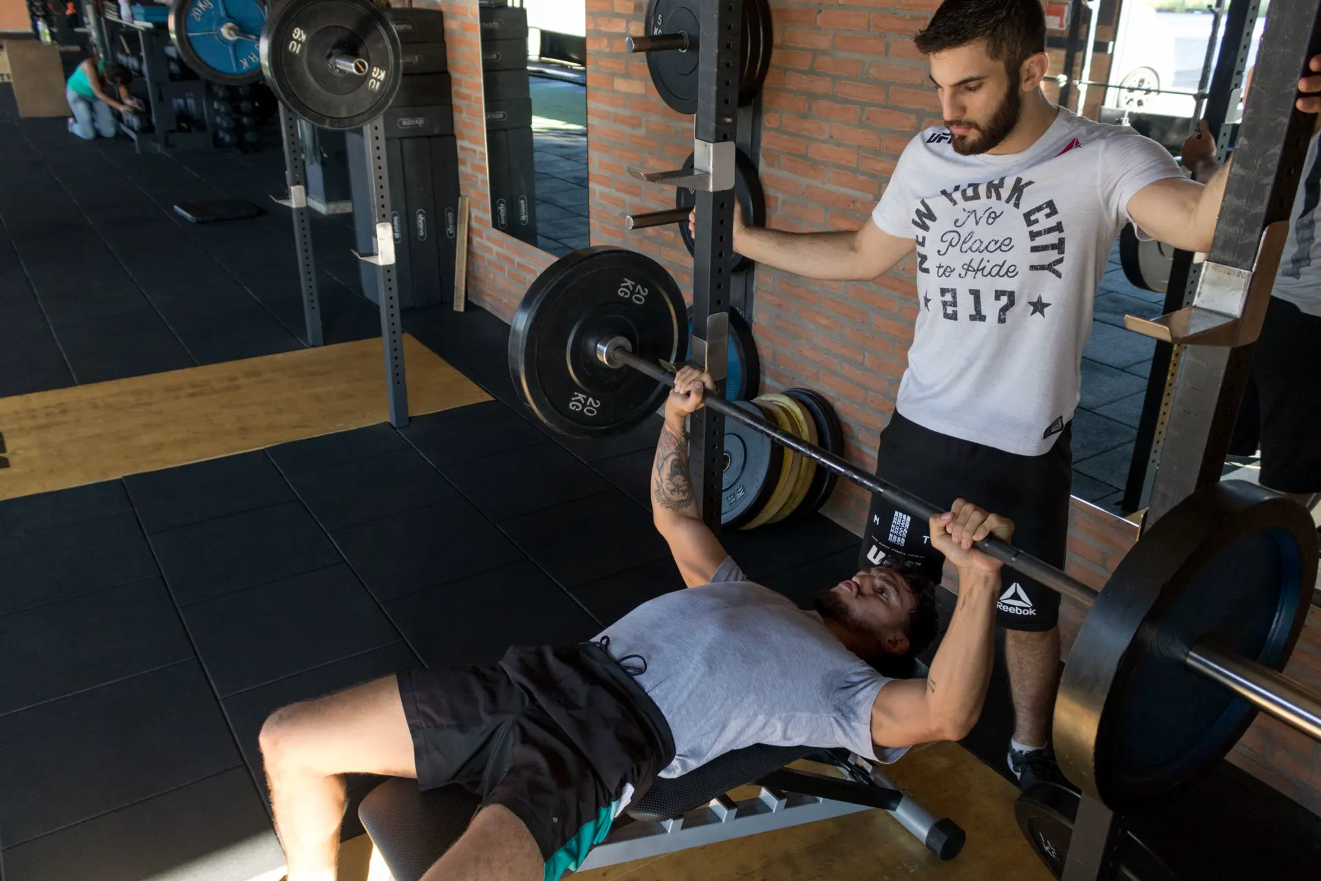 Powerlifting Programs for Meet Prep and Strength Powerlifter bench presses a heavy barbell while a spotter guards the bar in a strength gym